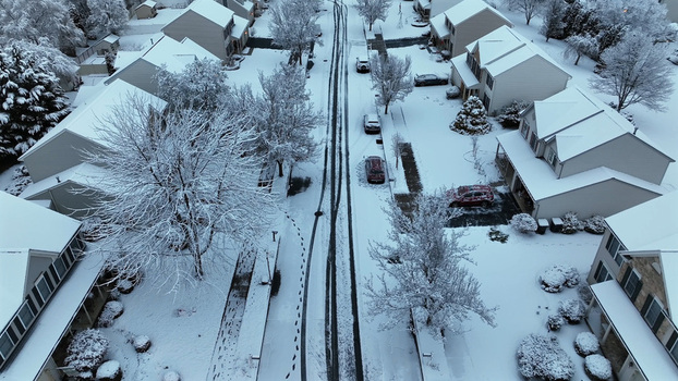 Aerial view of a residential street covered in fresh snow with tire tracks and footprints surrounded by houses and snow laden trees in Lititz Pennsylvania United States.