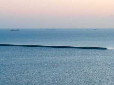 Aerial view of the Gulf of Gdansk featuring a long breakwater and cargo ships on the horizon under a soft hazy sky in Poland.