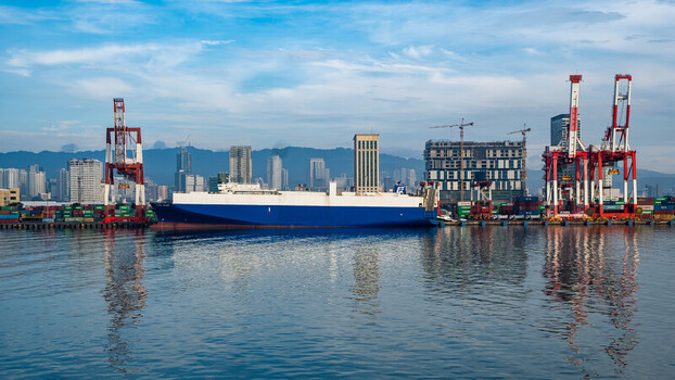 View of the Cebu Port Authority with a large cargo ship docked near industrial cranes and shipping containers against the Cebu City skyline in Central Visayas Philippines. View of the Cebu Port Authority with a large cargo ship docked near industrial cranes and shipping containers against the Cebu City skyline in Central Visayas Philippines.