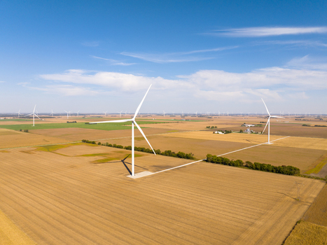 Aerial view of wind turbines standing in vast agricultural fields under a clear blue sky in Wolcott Indiana United States.