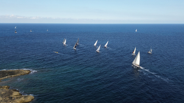 Aerial view of a sailing regatta with multiple sailboats navigating the deep blue Mediterranean sea near the rocky coastline of Valletta Port Region Malta. Aerial view of a sailing regatta with multiple sailboats navigating the deep blue Mediterranean sea near the rocky coastline of Valletta Port Region Malta.