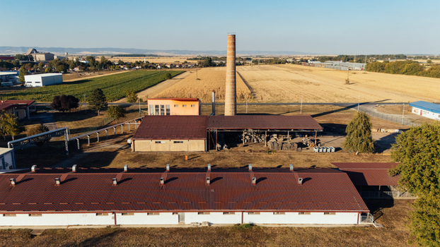Aerial view of an industrial facility with a tall brick chimney metal roofed buildings and surrounding agricultural fields in Sremska Mitrovica Vojvodina Serbia. Aerial view of an industrial facility with a tall brick chimney metal roofed buildings and surrounding agricultural fields in Sremska Mitrovica Vojvodina Serbia.