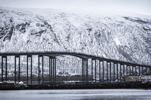 View of the Tromso Bridge spanning across the water with a massive snow covered mountain in the background Tromso Troms Norway. View of the Tromso Bridge spanning across the water with a massive snow covered mountain in the background Tromso Troms Norway.