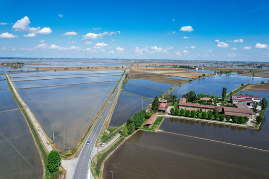 Aerial view of Abbazia di Lucedio surrounded by flooded rice fields and rural roads under a blue sky with scattered clouds in Trino Piemonte Italy.