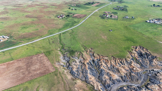 Aerial view of soil erosion dongas and a winding road through rural green fields and scattered homesteads Pietermaritzburg KwaZulu Natal South Africa.