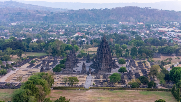 Aerial view of Prambanan Temple an ancient Hindu temple complex with towering stone spires surrounded by lush greenery and the town of Kecamatan Prambanan Daerah Istimewa Yogya Indonesia.