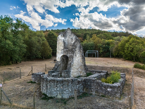 Aerial view of the medieval stone church ruins of Csabdi Hungary surrounded by woodland and a fenced clearing beneath dramatic clouds in late summer.