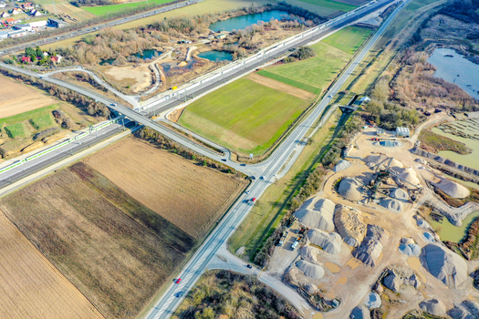 Aerial view of a major infrastructure construction site featuring new railway tracks and highway bridges surrounded by green fields and ponds near Buttenheim Bavaria Germany. Aerial view of a major infrastructure construction site featuring new railway tracks and highway bridges surrounded by green fields and ponds near Buttenheim Bavaria Germany.