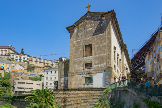 View of an ancient church with a cross atop stands weathered against a clear blue sky contrasting with the vibrant city landscape Porto Porto District Portugal. View of an ancient church with a cross atop stands weathered against a clear blue sky contrasting with the vibrant city landscape Porto Porto District Portugal.