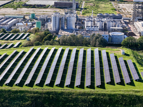 Aerial view of solar panels on a green hillside with an industrial plant and storage tanks in the background Crescentino Piedmont Italy. Aerial view of solar panels on a green hillside with an industrial plant and storage tanks in the background Crescentino Piedmont Italy.