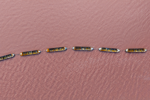 Aerial view of a chain of connected boats stand out against the vibrant pink hue of the water creating a striking contrast San Pedro del Pinatar Region of Murcia Spain. Aerial view of a chain of connected boats stand out against the vibrant pink hue of the water creating a striking contrast San Pedro del Pinatar Region of Murcia Spain.