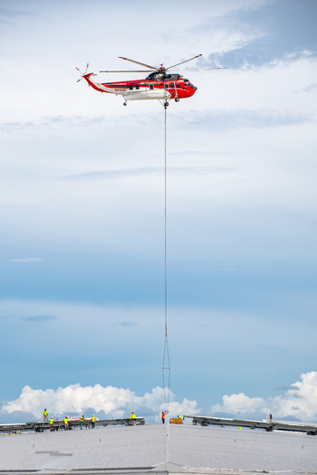 Miami Florida United States 22 September 2026 Aerial view of a helicopter lifting construction equipment onto the Kaseya Center roof with workers visible below.