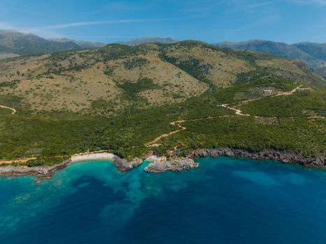 Aerial view of Aquarium Beach featuring turquoise waters rocky coves and lush green hills under a clear blue sky in Jala Vlore County Albania. Aerial view of Aquarium Beach featuring turquoise waters rocky coves and lush green hills under a clear blue sky in Jala Vlore County Albania.