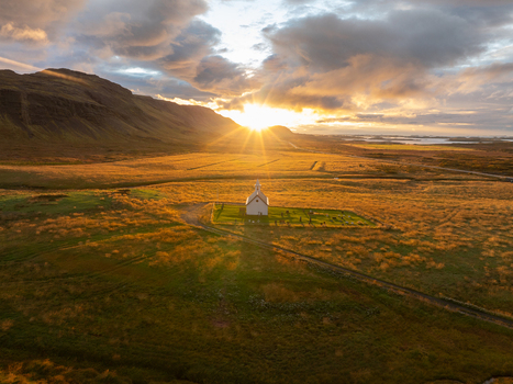 Aerial view of a solitary white church standing proudly in a vast grassy field illuminated by the radiant glow of the setting sun Snæfellsnes Iceland. Aerial view of a solitary white church standing proudly in a vast grassy field illuminated by the radiant glow of the setting sun Snæfellsnes Iceland.