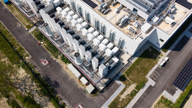 Aerial view of a modern hyperscale data center featuring rows of industrial cooling units solar panels and paved access roads in Melegnano Lombardy Italy.