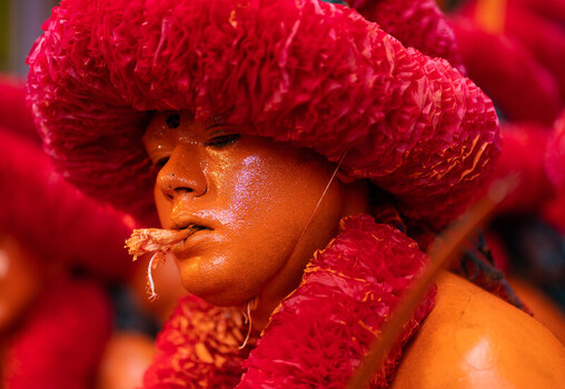 Munshiganj Bangladesh 13 April 2025 View of a person adorned in vibrant red headwear and garlands with their golden painted face glistening holding a piece of wood between their lips. Munshiganj Bangladesh 13 April 2025 View of a person adorned in vibrant red headwear and garlands with their golden painted face glistening holding a piece of wood between their lips.