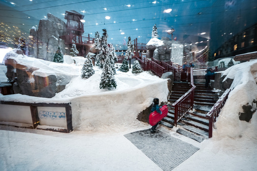 Dubai Dubai United Arab Emirates 20 April 2023 View of Ski Dubai featuring snow covered slopes pine trees and a child carrying a red sled on the stairs. Dubai Dubai United Arab Emirates 20 April 2023 View of Ski Dubai featuring snow covered slopes pine trees and a child carrying a red sled on the stairs.