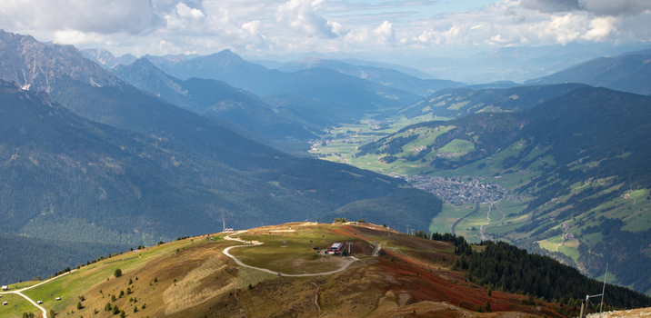 View of the Dolomites mountain range with grassy slopes winding paths and a valley town under a cloudy sky Rocca Pietore Veneto Italy. View of the Dolomites mountain range with grassy slopes winding paths and a valley town under a cloudy sky Rocca Pietore Veneto Italy.