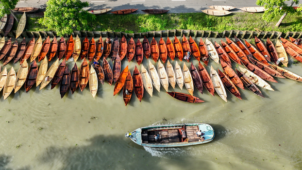 Aerial view of numerous small wooden boats some with people lined up along a riverbank contrasting with the water Pirojpur Pourashava Barisal Division Bangladesh. Aerial view of numerous small wooden boats some with people lined up along a riverbank contrasting with the water Pirojpur Pourashava Barisal Division Bangladesh.