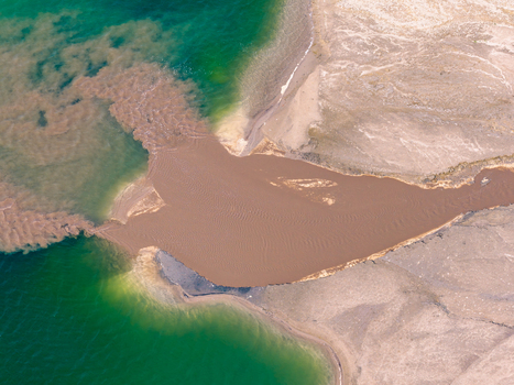 Aerial view of brown mineral sediment mixing with turquoise water in a post industrial lake in Poland.