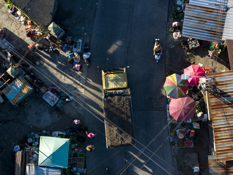 Aerial view of a yellow truck driving through a busy street market with colorful umbrellas and people Kemalang Central Java Indonesia.