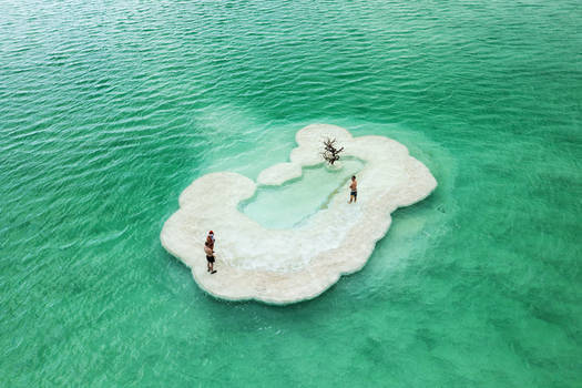 Aerial view of dramatic white salt formations resembling a sculpted cloud emerge from the vivid emerald waters creating a serene pool where figures relax Ein Bokek Israel. Aerial view of dramatic white salt formations resembling a sculpted cloud emerge from the vivid emerald waters creating a serene pool where figures relax Ein Bokek Israel.