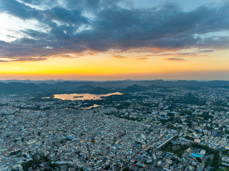Aerial view of the cityscape of Udaipur with Lake Pichola reflecting the golden sunset light surrounded by the Aravalli hills in Udaipur Rajasthan India.