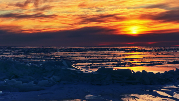 Aerial view of a vibrant sunset over a frozen icy landscape with dramatic clouds reflecting on the ice in Latvia. Aerial view of a vibrant sunset over a frozen icy landscape with dramatic clouds reflecting on the ice in Latvia.
