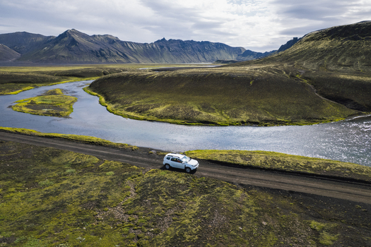 Aerial view of a white SUV driving on the F235 road through a volcanic landscape with a winding river and mossy green mountains Highlands of Iceland Iceland. Aerial view of a white SUV driving on the F235 road through a volcanic landscape with a winding river and mossy green mountains Highlands of Iceland Iceland.