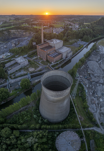 Aerial view of the abandoned power plant with its iconic cooling tower and industrial buildings at sunset surrounded by trees and a river in Charleroi Wallonia Belgium.