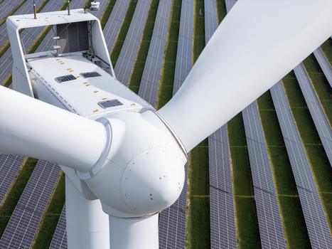Aerial view of a large white wind turbine standing in front of rows of solar panels in a renewable energy farm in Poland.