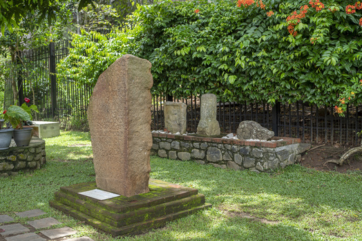 View of an ancient stone inscription stele standing on a mossy brick base in the lush gardens of the Sri Dalada Maligawa complex in Kandy Central Province Sri Lanka. View of an ancient stone inscription stele standing on a mossy brick base in the lush gardens of the Sri Dalada Maligawa complex in Kandy Central Province Sri Lanka.