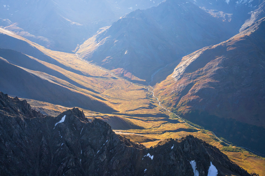 Aerial view of Chugach State Park featuring rugged mountain peaks deep valleys a winding stream and golden autumn tundra in Anchorage Alaska United States. Aerial view of Chugach State Park featuring rugged mountain peaks deep valleys a winding stream and golden autumn tundra in Anchorage Alaska United States.
