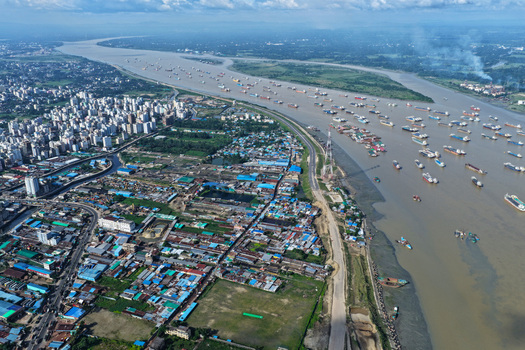 Aerial view of Karnaphuli River flowing past the dense urban landscape of Chattogram with numerous cargo ships anchored in the water in Chattogram Chittagong Division Bangladesh.