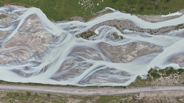 Aerial view of the braided Enilchek River with glacial sediment patterns and gravel bars flowing alongside a dirt road in Enilchek Issyk Kul Region Kyrgyzstan. Aerial view of the braided Enilchek River with glacial sediment patterns and gravel bars flowing alongside a dirt road in Enilchek Issyk Kul Region Kyrgyzstan.