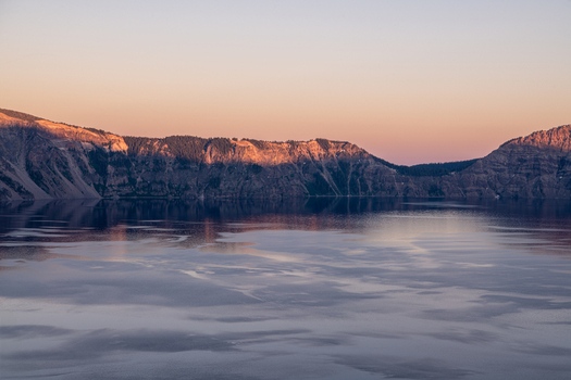 View of the serene lake reflecting the soft light of the sunset illuminating the rugged cliffs creating a tranquil scene Crater Lake Oregon United States. View of the serene lake reflecting the soft light of the sunset illuminating the rugged cliffs creating a tranquil scene Crater Lake Oregon United States.