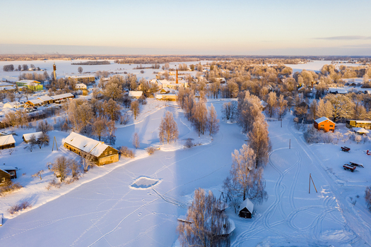 Aerial view of a frozen river winding through a snow covered landscape with frost laden trees and small rural buildings under a clear winter sky in Latvia. Aerial view of a frozen river winding through a snow covered landscape with frost laden trees and small rural buildings under a clear winter sky in Latvia.