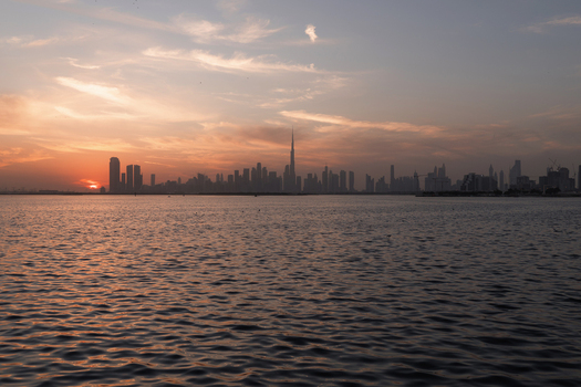 View of the sun setting behind the Dubai skyline casting a warm glow over the water with the Burj Khalifa standing tall Dubai United Arab Emirates.