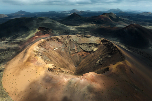 Aerial view of a massive volcanic crater with reddish soil and rugged slopes in a vast lava field under a cloudy sky Lanzarote Canarias Spain. Aerial view of a massive volcanic crater with reddish soil and rugged slopes in a vast lava field under a cloudy sky Lanzarote Canarias Spain.