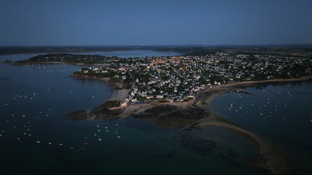 Aerial view of the coastline where the tranquil sea meets the sandy shore illuminating the clustered buildings Carantec Bretagne France.