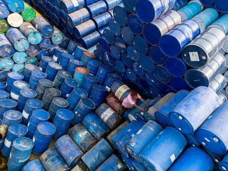 Aerial view of a worker navigating through massive stacks of blue and multi colored industrial metal drums in a storage yard Dhaka Dhaka Division Bangladesh. Aerial view of a worker navigating through massive stacks of blue and multi colored industrial metal drums in a storage yard Dhaka Dhaka Division Bangladesh.