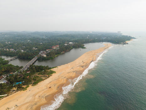 Aerial view of a sandy beach separating the ocean from a river estuary with a bridge and lush tropical vegetation in Galle Southern Province Sri Lanka.