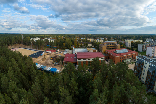 Aerial view of a school complex with a red roof an adjacent sports field under construction and surrounding pine forests in a residential area in Latvia. Aerial view of a school complex with a red roof an adjacent sports field under construction and surrounding pine forests in a residential area in Latvia.