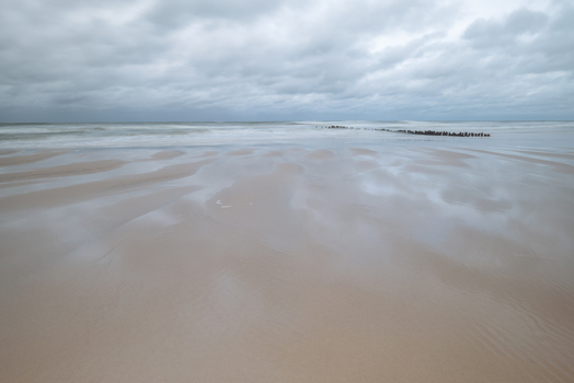 View of a wide sandy beach with wet reflections under a heavy overcast sky and waves crashing along the Baltic Sea coast Debki Pomeranian Voivodeship Poland. View of a wide sandy beach with wet reflections under a heavy overcast sky and waves crashing along the Baltic Sea coast Debki Pomeranian Voivodeship Poland.