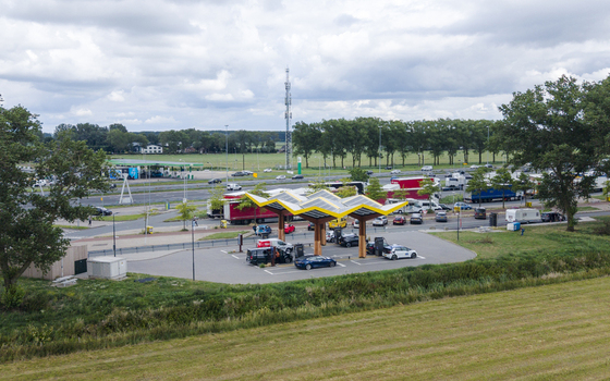 Aerial view of Fastned Charging Station with electric vehicles parked under the solar canopy surrounded by green fields and a highway in Breukelen Utrecht Netherlands. Aerial view of Fastned Charging Station with electric vehicles parked under the solar canopy surrounded by green fields and a highway in Breukelen Utrecht Netherlands.