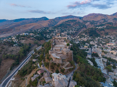 Aerial view of Gjirokaster Castle with its historic stone fortifications and surrounding town architecture set against a mountainous landscape in Gjirokaster Gjirokaster County Albania. Aerial view of Gjirokaster Castle with its historic stone fortifications and surrounding town architecture set against a mountainous landscape in Gjirokaster Gjirokaster County Albania.