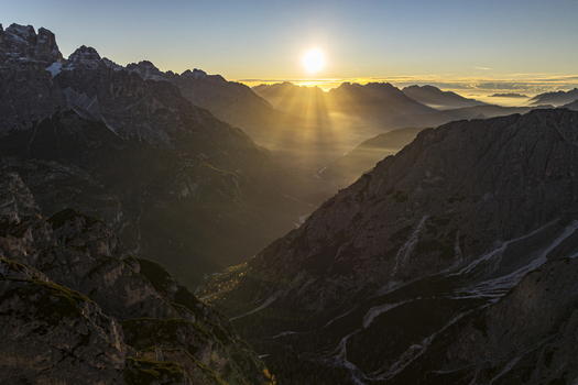 Aerial view of the sun s radiant rays piercing through the rugged peaks casting shadows and illuminating the valleys below Auronzo di Cadore Veneto Italy. Aerial view of the sun s radiant rays piercing through the rugged peaks casting shadows and illuminating the valleys below Auronzo di Cadore Veneto Italy.
