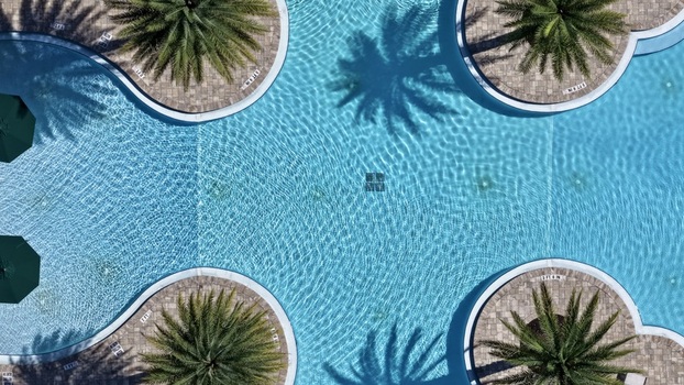 Aerial view of a swimming pool with clear blue water surrounded by four circular stone decks with palm trees and green umbrellas in St. Johns County Florida United States. Aerial view of a swimming pool with clear blue water surrounded by four circular stone decks with palm trees and green umbrellas in St. Johns County Florida United States.