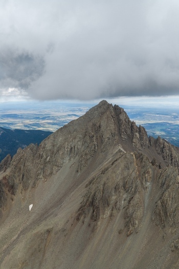 Aerial view of Mount Sneffels in the San Juan Mountains featuring rugged rocky slopes and a dramatic cloud formation over the summit in Ouray County Colorado United States. Aerial view of Mount Sneffels in the San Juan Mountains featuring rugged rocky slopes and a dramatic cloud formation over the summit in Ouray County Colorado United States.