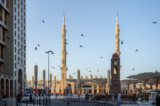 View of Al Masjid e Nabawi with its iconic minarets large umbrellas and birds flying in the courtyard in Madinah Al Madinah Province Saudi Arabia.
